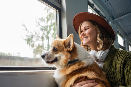 Smiling woman looking through window with dog while travelling in train