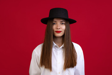 Stylish young beautiful girl wearing black hat isolated on dark studio background in neon light. Concept of emotions, fashion