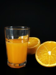 glass of orange juice on black background with two half of oranges with copy space