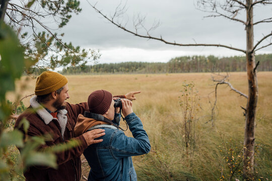 Father pointing while standing by boy bird watching through binoculars in forest