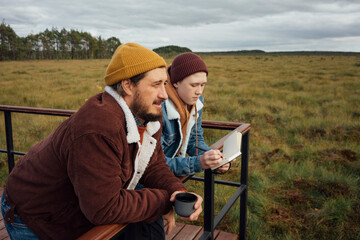 Boy writing in diary while leaning on railing with father