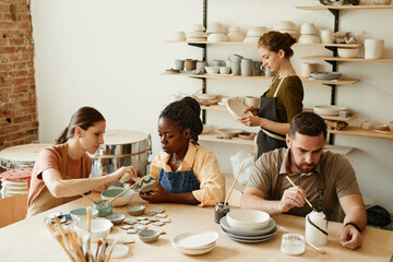 Warm toned portrait of diverse group of people enjoying pottery workshop in cozy studio - obrazy, fototapety, plakaty