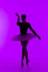 Fototapeta na wymiar Beautiful ballerina on purple background dancing ballet. Woman performs smooth movements. Sensual dancer in tutu dress on scene under neon light.. 