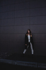 Sexy girl posing against a dark wall in the evening. An elegant fashionable girl in a long black...