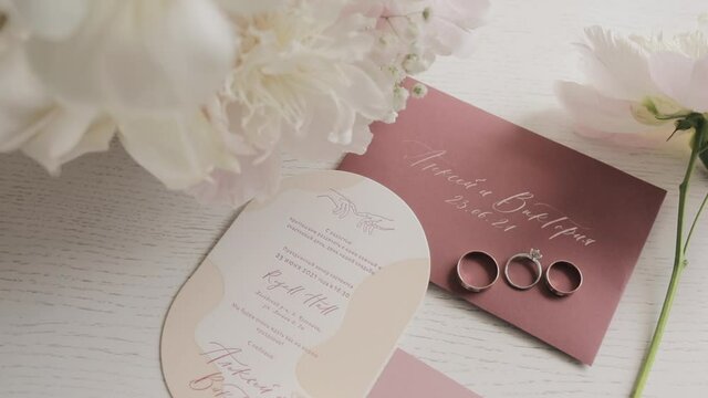 wedding rings and white pions bouquet lying on the invitation card