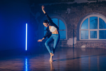 Young woman in casual style - jeans and leather jacket doing ballet in modern studio. Attractive...