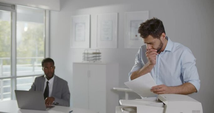 Portrait of sick office worker using copy machine with colleague looking worried