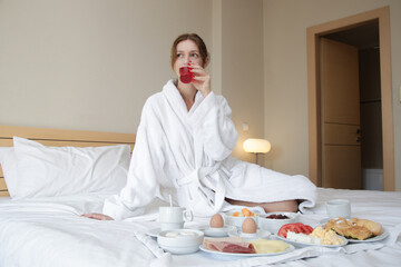 Young woman enjoying breakfast in the bed. 
Calm idyllic morning at home or hotel room.