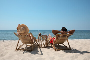 Couple resting in wooden sunbeds on tropical beach
