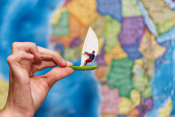 A child's hand holds a toy windsurfer against background of a world map