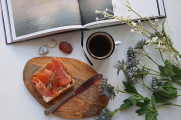 cup of coffee with salmon sandwich near a book