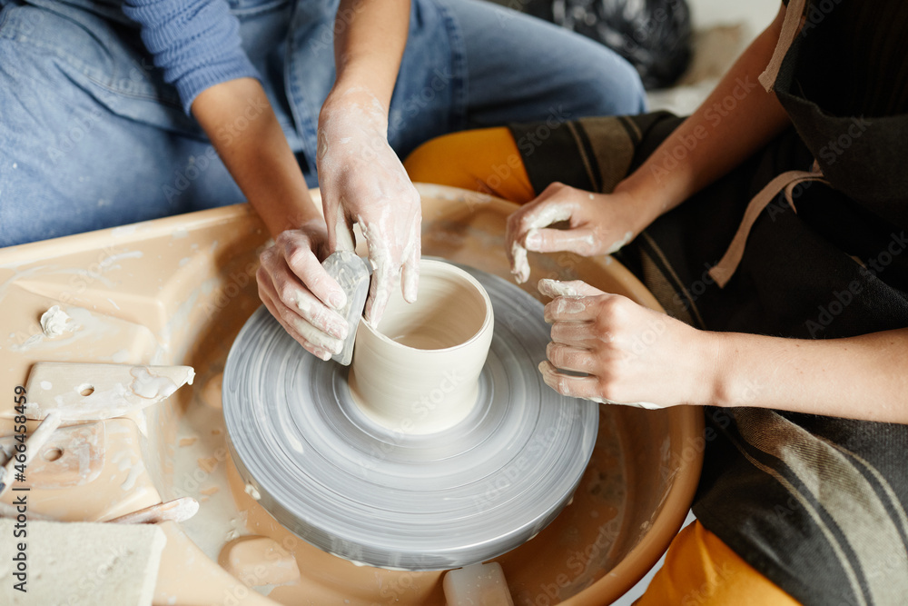 Wall mural Close up of two young women working on pottery wheel together in handmade ceramics workshop, copy space