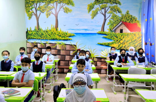 Students wearing protective masks sit in a classroom on the first day of new term at a primary school in Baghdad