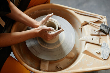 Top view close up of young woman working on pottery wheel together in handmade ceramics workshop,...