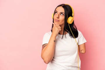 Young caucasian woman with one arm listening to music isolated on pink background looking sideways with doubtful and skeptical expression.