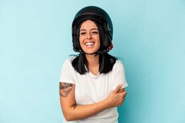 Young caucasian woman with one arm wearing a motorcycle helmet isolated o blue background laughing and having fun.