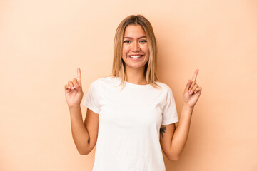 Young caucasian woman isolated on beige background indicates with both fore fingers up showing a...