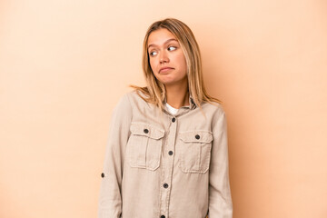 Young caucasian woman isolated on beige background shrugs shoulders and open eyes confused.
