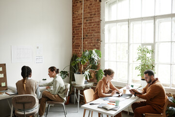 Wide angle portrait of diverse creative team working in modern studio lit by sunlight, copy space