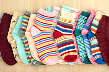 Many socks are stacked in a row. Knitted clothes in the form of socks. Bright multi-colored socks on a wooden background.