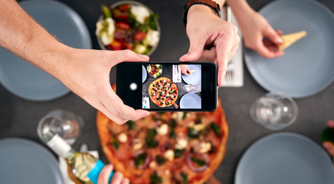 Overhead View Of Friends In Pizza Restaurant Taking Picture Of Food On Mobile Phone