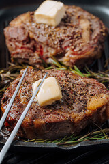 cooking sumptuous steaks in a grill pan with butter spreading over the steak seasoned with ground pepper and salt with rosemary sprigs