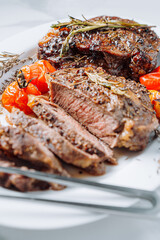 juicy well-fried ribeye steaks on a white platter on a white marble surface with raspmarine and fried cherry tomatoes and peppers. steaks are sliced and ready to serve