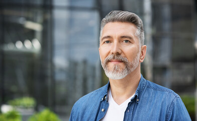 Handsome smiling mature man closeup portrait. Cheerful middle age man looking at camera in a city...