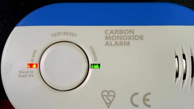 Closeup POV shot of a finger tip pressing the button to test the operation of  a household carbon monoxide alarm, with red and green lights flashing.