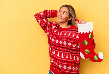 Young caucasian woman holding a elf sock isolated on yellow background touching back of head, thinking and making a choice.