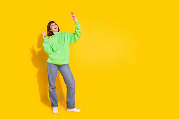 Full length body size view of beautiful cheerful girl making selfie showing v-sign isolated over bright yellow color background