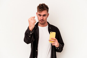 Young caucasian man holding a mobile phone isolated on white background showing fist to camera, aggressive facial expression.