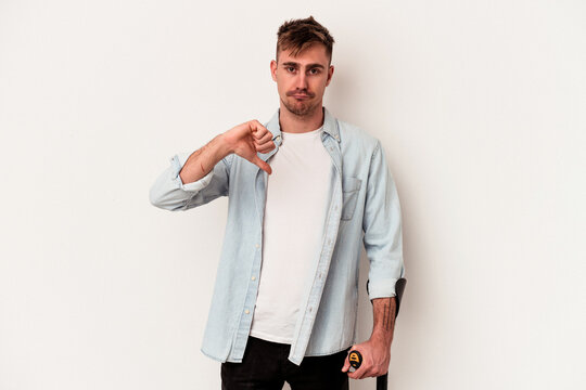 Young caucasian man holding crutch isolated on white background showing a dislike gesture, thumbs down. Disagreement concept.