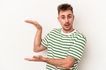 Young caucasian man isolated on white background shocked and amazed holding a copy space between hands.