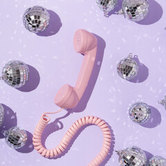 Christmas and New Year creative layout with disco ball decoration and pink retro phone handset on pastel purple background. 80s or 90s aesthetic fashion concept. Minimal Valentines day idea.
