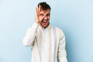 Young caucasian man isolated on blue background excited keeping ok gesture on eye.