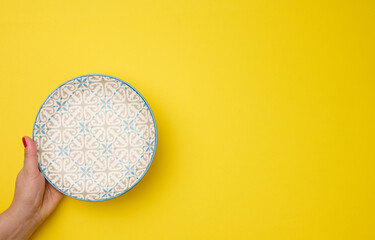 female hand holding an empty round plate on a yellow background, top view