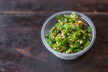 Chopped green chili put in a clear plastic cup on the wooden table. It’s a spicy topping added with sukiyaki or shabu sauce.