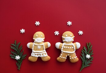 Gingerbread couple with protective face masks on red background with decoration. Original Christmas or New Year greeting card
