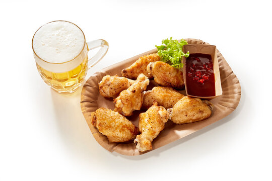 Chicken wings and ketchup served on white background with glass of lager beer
