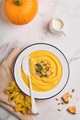 Pumpkin traditional soup with creamy silky texture with sage leaves and red pepper in white plate or bowl. Light grey background. Copy space. Mock up. Top view, flat lay.