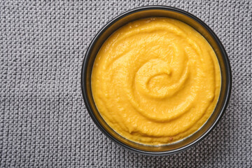 Pumpkin traditional soup with creamy silky texture with sage leaves and red pepper in black plate or bowl. Old grey background. Copy space. Mock up. Top view, flat lay.