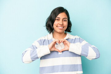 Young latin woman isolated on blue background smiling and showing a heart shape with hands.