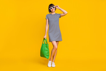 Full body photo of funky brunette millennial lady wear striped dress spectacles bag sneakers isolated on yellow background