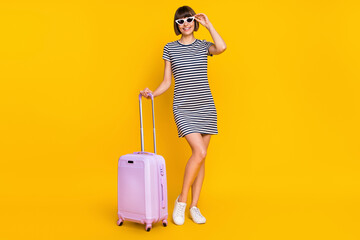 Full size photo of funky brunette millennial lady stand with bag wear dress sneakers eyewear isolated on yellow background