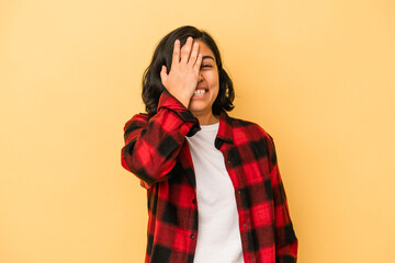 Young latin woman isolated on yellow background having fun covering half of face with palm.