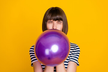 Photo of impressed brunette millennial lady blow balloon closed eyes wear blue t-shirt isolated on yellow background