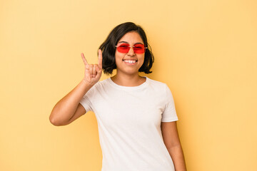Young latin woman isolated on yellow background showing a horns gesture as a revolution concept.