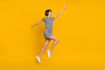 Fototapeta na wymiar Full length photo of funky millennial lady jump wear striped dress sneakers isolated on yellow background