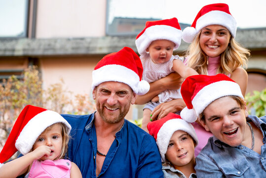 merry christmas! young large family portrait celebrating xmas wearing a santa hat outdoors. parents and children close up during winter warm festivities. family time on summer vacation holiday concept